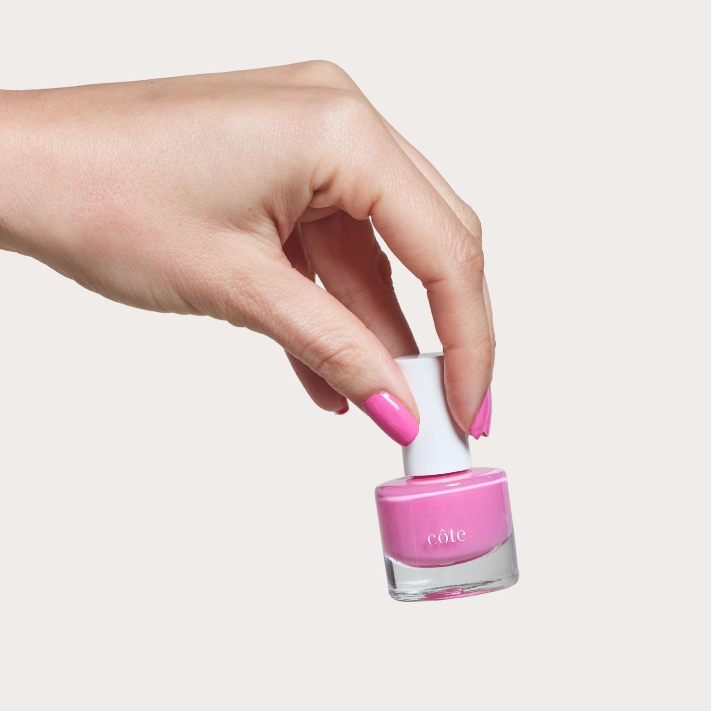 Hand holding Côte Beauty Hotshot True Bright Pink Non-Toxic Nail Polish with nails painted. 