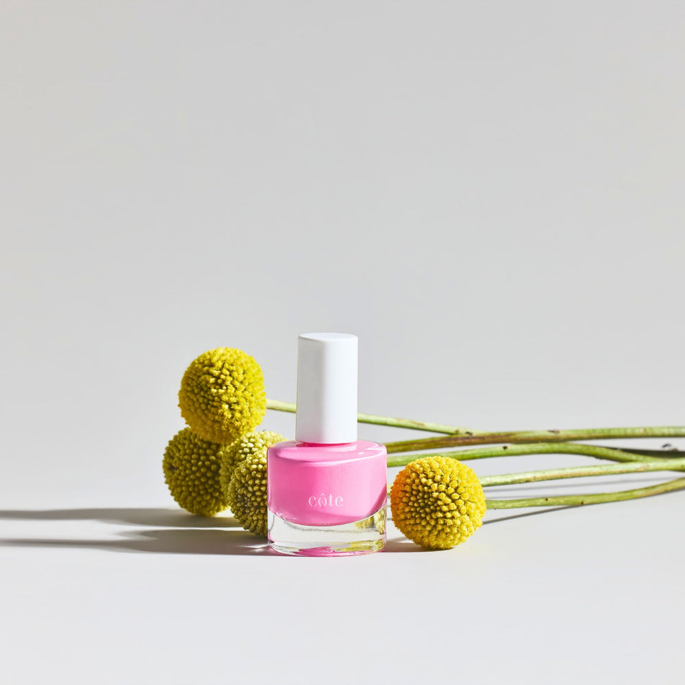 Côte Beauty Hotshot True Bright Pink Non-Toxic Nail Polish bottle with florals in the background.