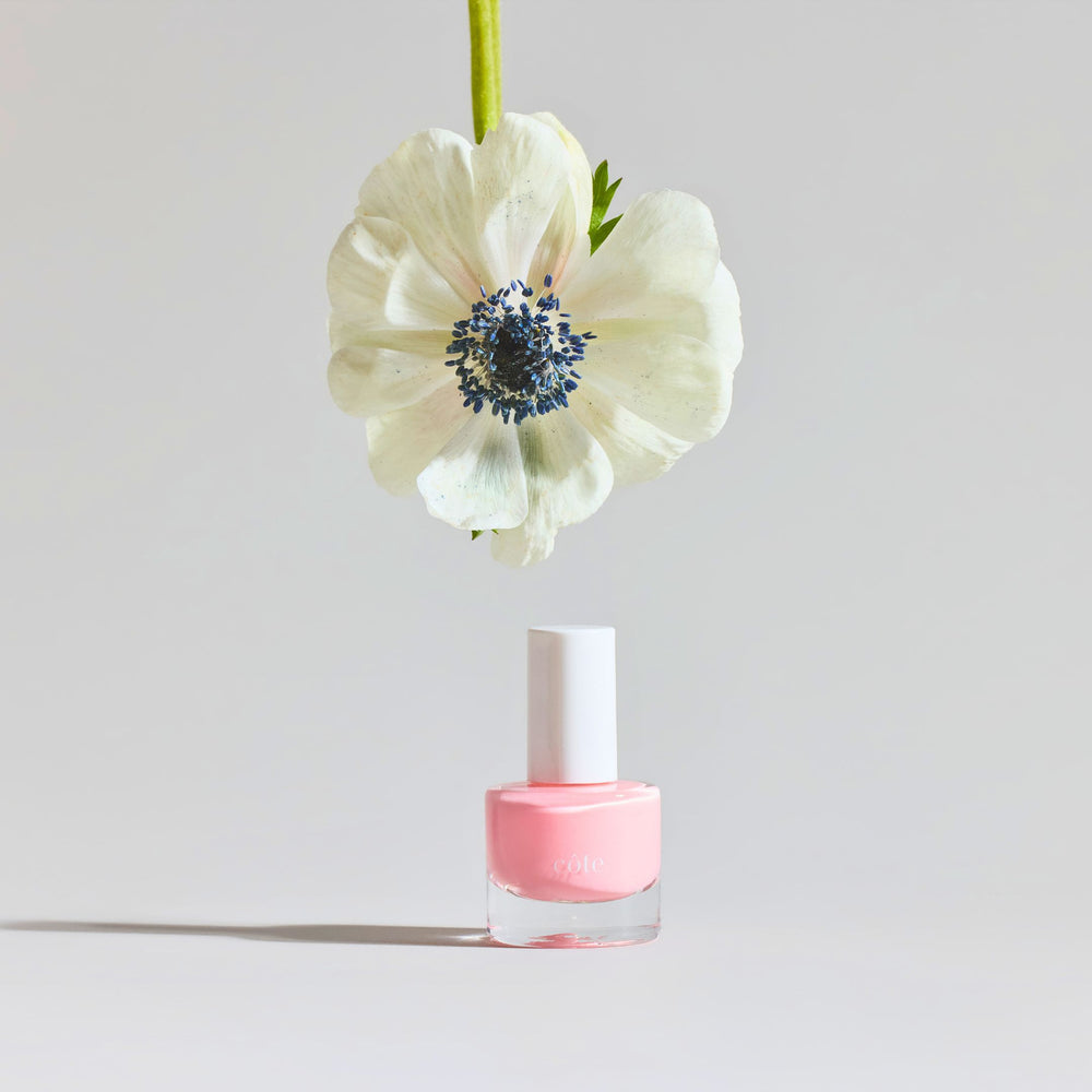 Côte Beauty Pink Clouds Sheer Petal Blush Non-Toxic Nail Polish bottle with floral in background. 