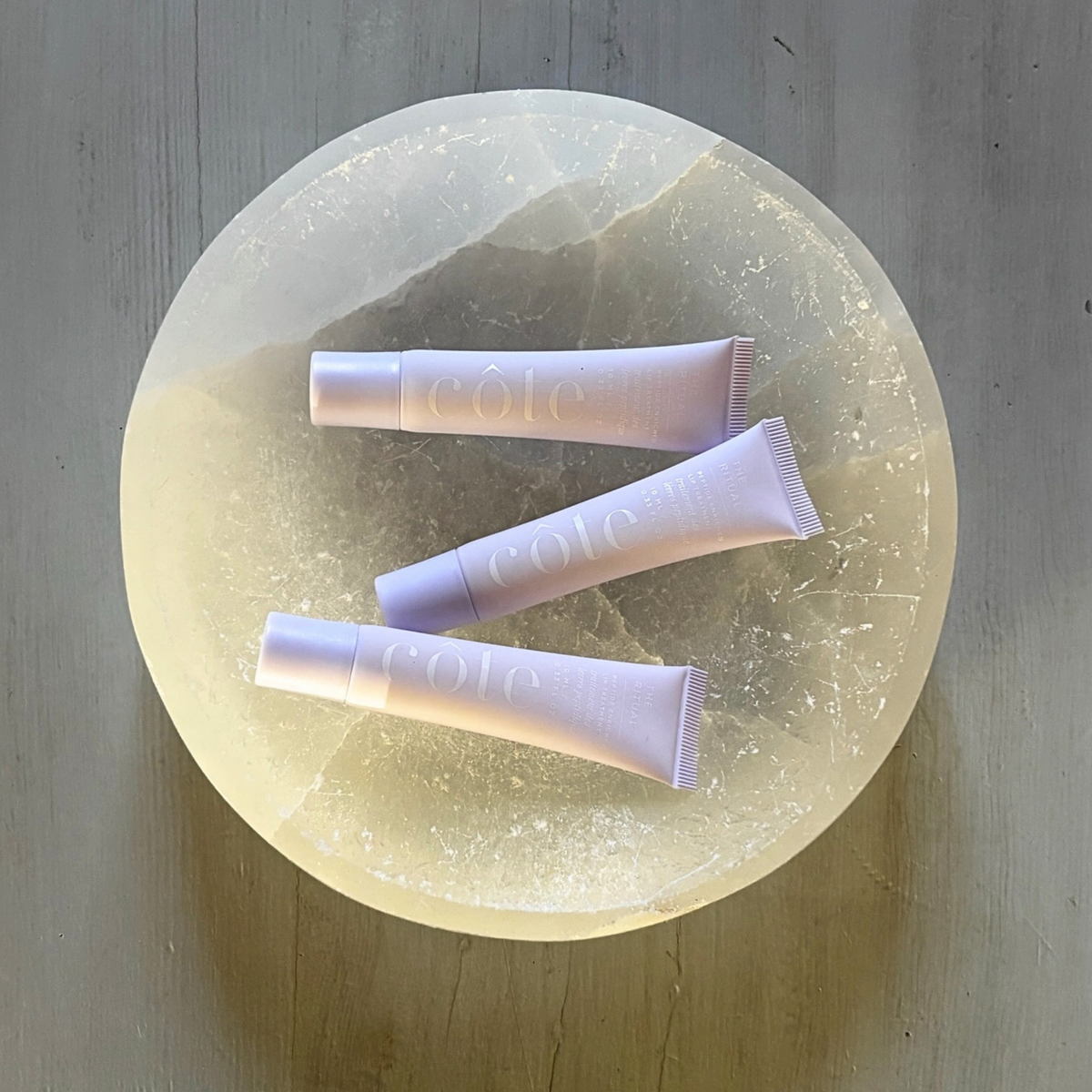 Three tubes of Côte Beauty The Ritual Peptide Lip Treatment Non-Toxic Hydrating Lip Care on a marble tray.