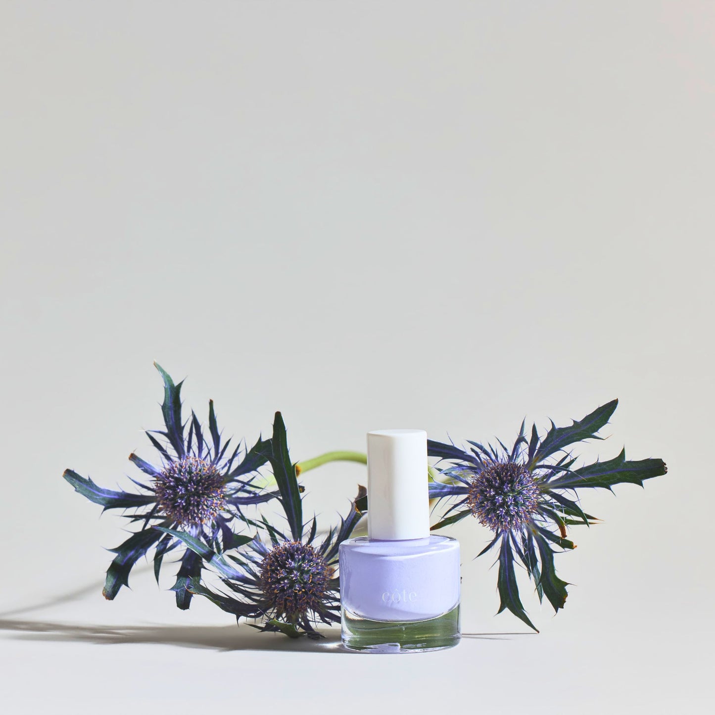 Côte Beauty Sugar Côte Soft Lavender Non-Toxic Nail Polish bottle with florals in the background.