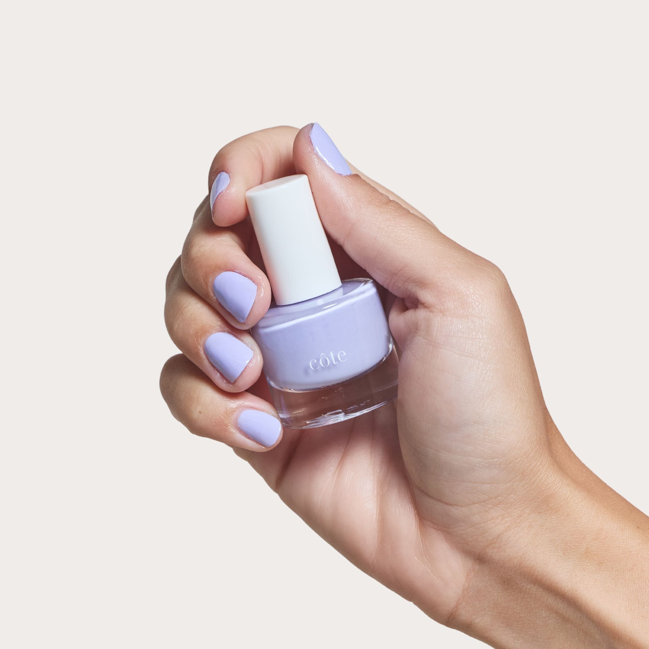 Hand holding Côte Beauty Sugar Côte Soft Lavender Non-Toxic Nail Polish bottle with nails painted. 