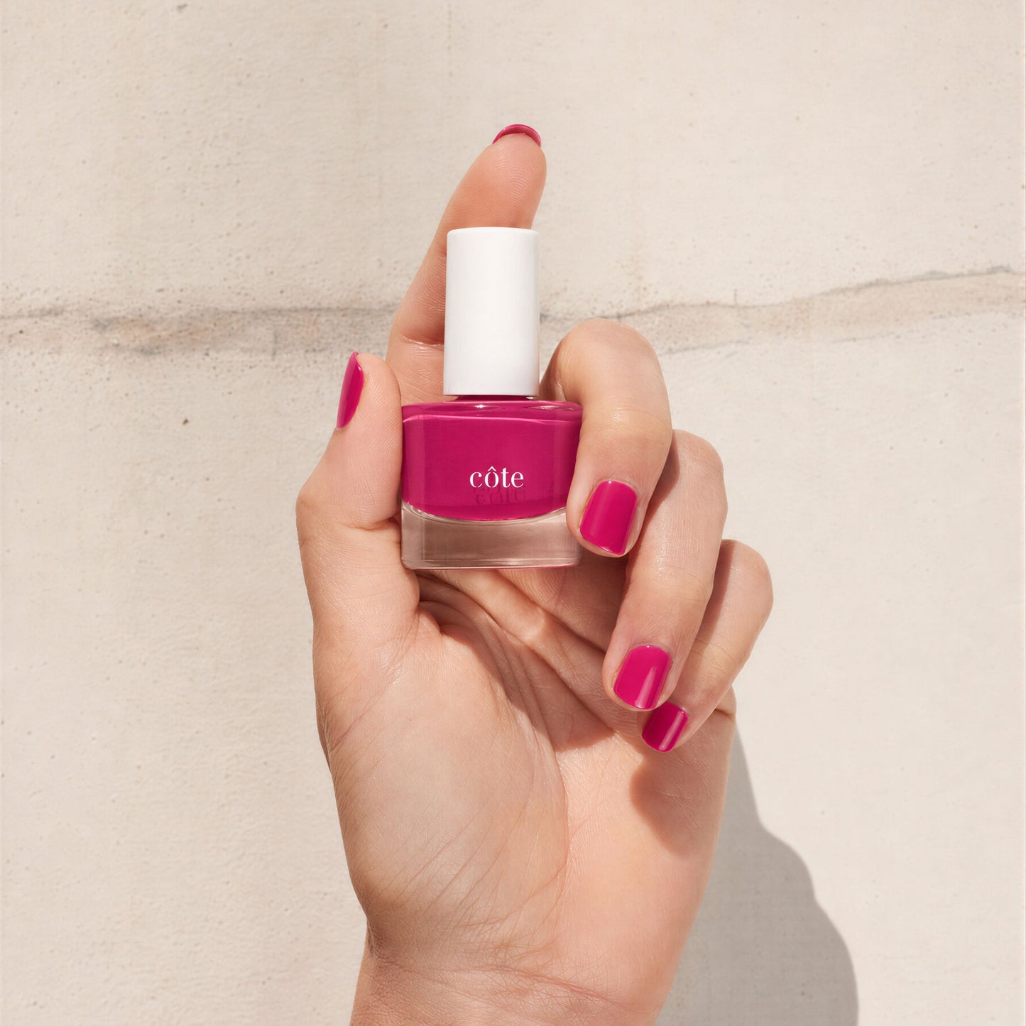 Hand holidng Côte Beauty Velvet Rose Lush Berry Pink Non-Toxic Nail Polish bottle with nails painted to match.