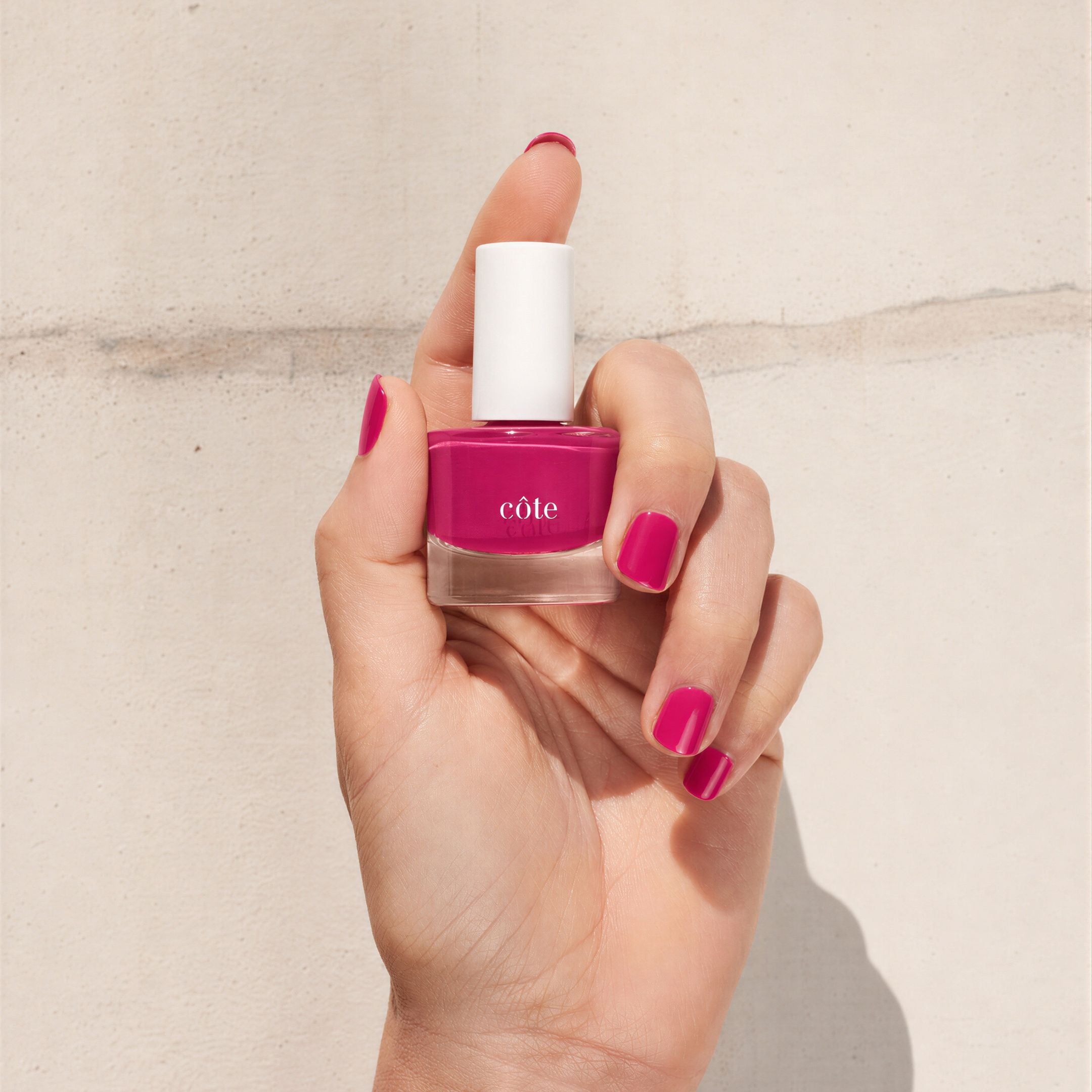 Hand holidng Côte Beauty Velvet Rose Lush Berry Pink Non-Toxic Nail Polish bottle with nails painted to match.
